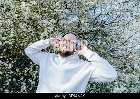 Happy kind bearded man wearing headphones near blooming tree in spring Stock Photo