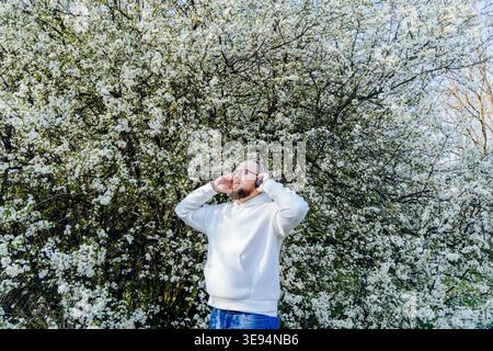 Bearded man wearing headphones near blooming tree in spring Stock Photo