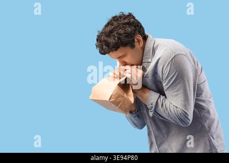 Young man with paper bag having panic attack on blue background Stock Photo
