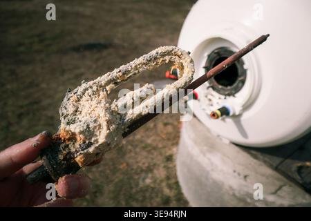 Plumber hand hold the heating element after long-term use, covered with deposits from hard water. Replacing a heating element damaged by scale and lim Stock Photo