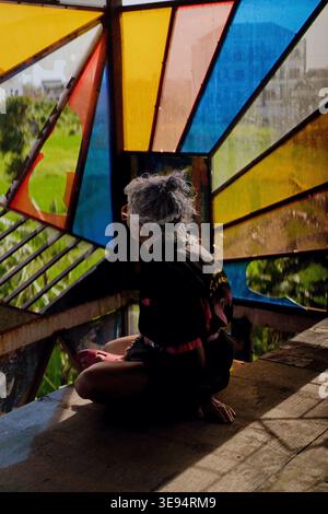 Mature woman from behind sitting in colorful art pavilion, Bali Stock Photo