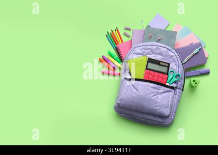 Lilac school backpack with different stationery supplies on green background Stock Photo