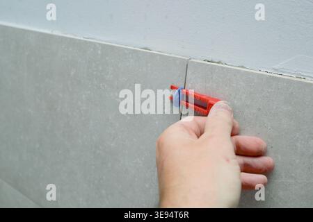Tiler's hand installing leveling system tiles. Leveling system wedges for tiles. Worker Places New Tile Stock Photo