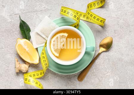 Cup of diet tea, lemon and measuring tape on grunge background. Weight loss concept Stock Photo