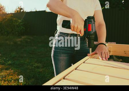 Female carpenter at work using hand drilling machine. Female carpenter building a wooden cabinet with an electric drill Stock Photo