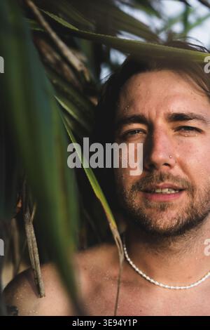Young man with glitter face peeking through palm leaves, Bali Stock Photo