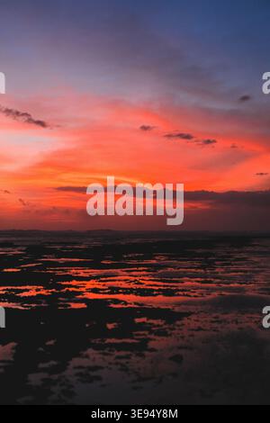 Vivid fiery orange and red sunset over rocky tidal flats and ocean Stock Photo