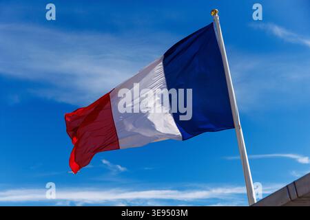 A close-up of the blue, white, and red tricolor flag of France rippling under a bright, sunny sky. Stock Photo