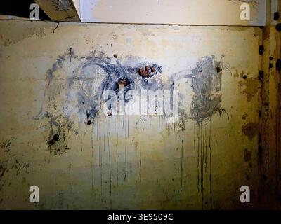 Abstract paint drips streak down a weathered, yellowed wall. Dark splotches mar the faded, cracked plaster surface. Rust stains cling to the corner, h Stock Photo