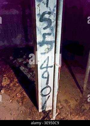 Weathered concrete post marked with faded numbers. Grungy urban scene with dirt and shadows. Post stands tall against dim, gritty background. Handwrit Stock Photo