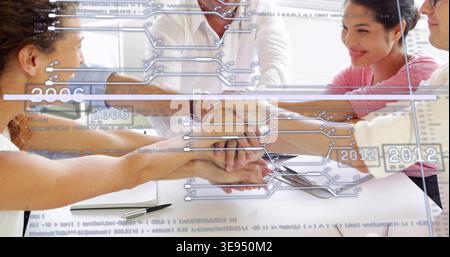 Joining five colleagues in light shirts placing stacked hands on white table at office with tablet Stock Photo