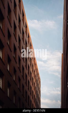 Modern red brick apartment buildings at golden hour. A low-angle shot of a two parallel brick residential building in rays of warm sunset light. Stock Photo
