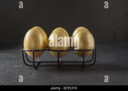 Chicken golden eggs in stand on black background. Easter dark concept. Close up. Stock Photo