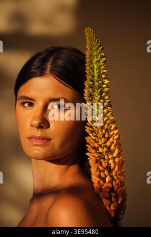 Dark-haired female model poses elegantly with a unique plant accent, highlighting her features and the interplay of light and shadow in a serene atmosphere Stock Photo