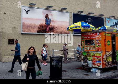 A woman walks past a food cart while people stroll along a sidewalk next to a large billboard featuring a person on a horse. Stock Photo