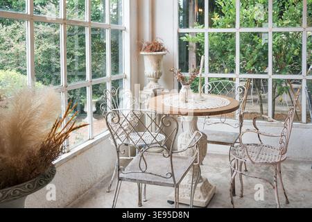 Interior of empty vintage table and chairs by the window among the tropical garden in coffee shop Stock Photo