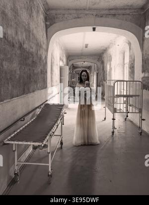 old abandoned Hospital corridor with sick bed in a lost place sanatorium and ghost woman with baby and nightglown spooky vibes Stock Photo