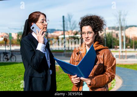 Business women collaborating outdoors discussing project details Stock Photo