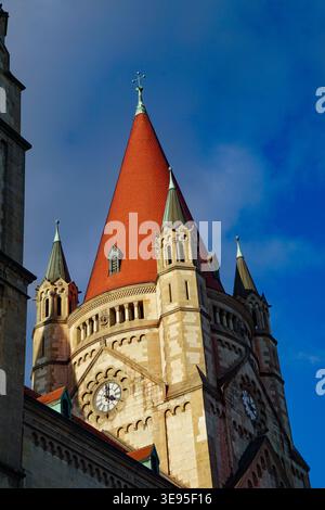 Historic church tower with red tiled spire and clock rises against blue sky with clouds in close-up architectural exterior view. Stock Photo