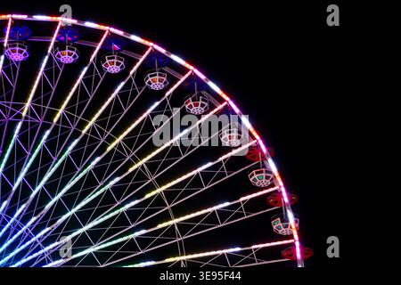 Ferris wheel with illuminated cabins and multicolored lights captured at night against dark sky at amusement park Stock Photo