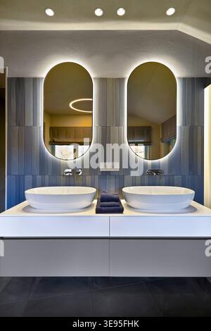 Front view of bathroom vanity with double vessel sinks, stainless steel faucet and curved rectangular mirrors in renovated 19th-century villa Stock Photo