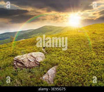 mountain landscape during summer at sunset. alpine meadows on green slopes and hills in evening light. amazing adventure scenery under rainbow. explor Stock Photo