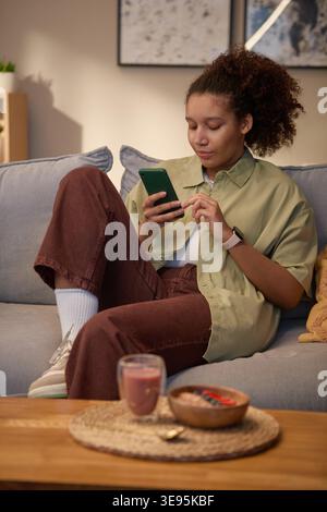 Black Woman Using Smartphone While Relaxing at Home during Breakfast Stock Photo