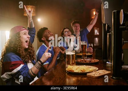 Diverse Friends Cheering While Watching Sports Broadcast in Bar Stock Photo