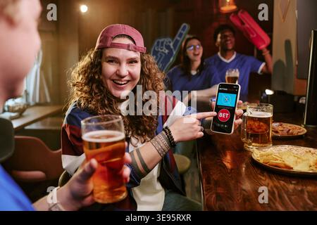 Portrait of Adult Woman Showing Sports Betting App in Bar Stock Photo