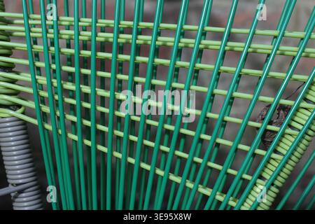 Close-up of woven green plastic chair back with vertical slats and horizontal weave pattern, shallow depth of field, abstract texture background. Stock Photo