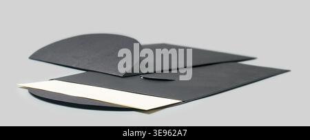 two matte black paper envelopes with blank white card partially tucked inside on grey background, side view with soft focus, elegant premium mailing Stock Photo
