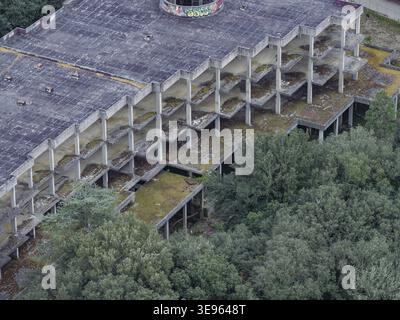 Aerial view of an abandoned concrete building frame with multiple floors and pillars surrounded by lush green trees in Leccio, Tuscany, Italy. Stock Photo