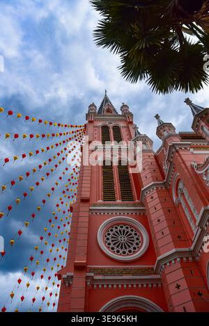 Towering pink church with ornate Gothic architecture. Colorful star banners hang against dramatic cloudy sky. Green palm fronds frame the top right. I Stock Photo