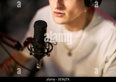Close up of young adult streamer speaking into podcast microphone while recording live content with headphones. Ideal for creator economy, audio production, social media marketing Stock Photo