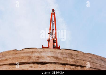 Low angle view of a construction crane rising above the top of a curved concrete tower against a bright blue sky. Industrial construction and engineer Stock Photo