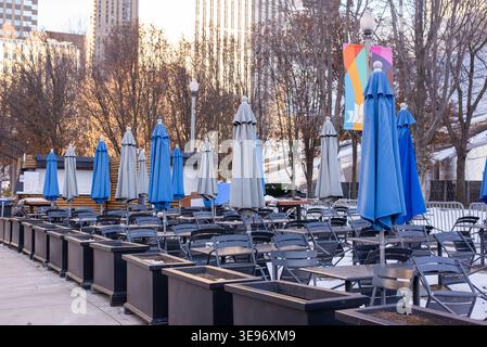 Empty outdoor cafe seating area with rows of chairs and closed umbrellas in urban park during cold season. No people. Stock Photo