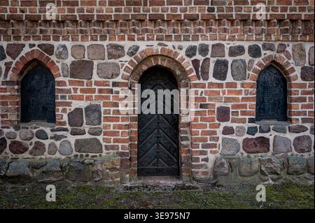 Arched wooden door with two narrow pointed‑arch window openings in the fieldstone and brick wall of the historic church in Lindenberg. Stock Photo