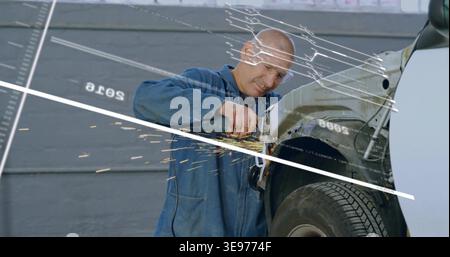 Grinding mechanic using grinder in garage, blue overalls and goggles, sparks hitting damaged fender Stock Photo