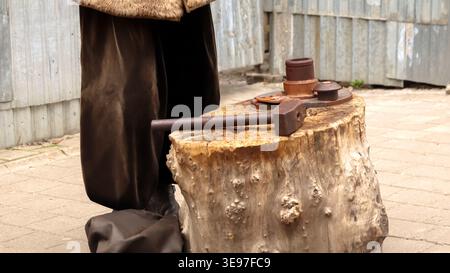 Close-up of a large old hammer lying on a tree stump anvil. Historical reenactment of traditional coin minting or blacksmithing outdoors. Craftsmans t Stock Photo
