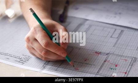 Close-up of a hand drawing an architectural plan on graph paper with a green pencil. Professional architect or engineer working on a technical Stock Photo