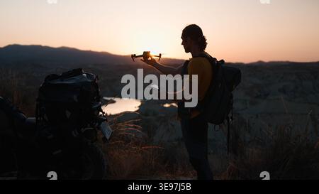 Adventurer preparing drone for flight at sunset over scenic desert landscape Stock Photo