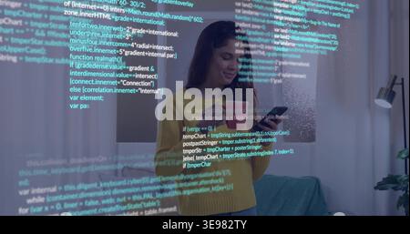 Standing woman wearing mustard knit sweater, holding tablet in living room with projected code Stock Photo