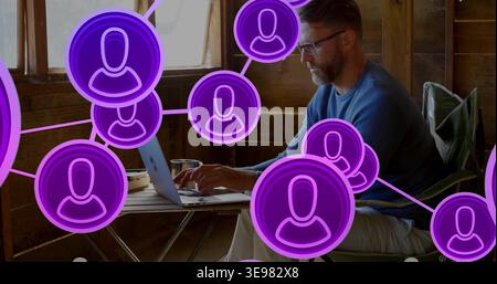 Typing man wearing blue sweater and glasses using laptop in cabin with purple avatars, copy space Stock Photo