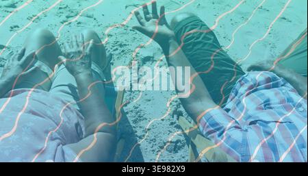 Sitting man and woman wearing casual clothes on beach in folding chairs, footprints, teal overlay Stock Photo