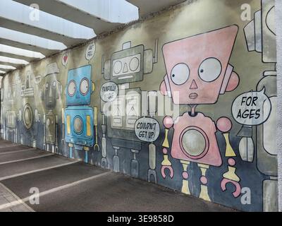 Colorful robot mural painted on underpass wall. Pink and blue robots with speech bubbles. Cartoon style art for all ages. Large eyes and simple design Stock Photo