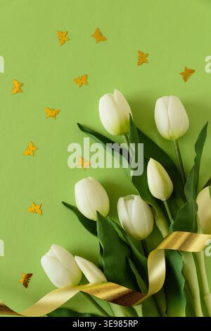 Elegant spring composition featuring white tulips arranged with butterflies confetti on a soft green background with a flowing satin ribbon. Easter or Stock Photo