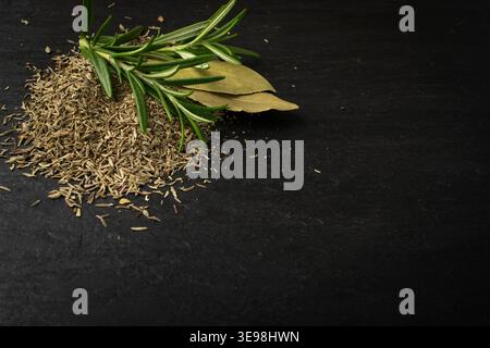 Pile of dry chopped thyme on black food slate background. Dried crushed oregano leaves. Ground thymus seasoning, fresh green rosemary herbs and spices Stock Photo