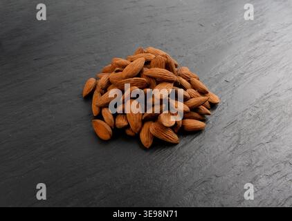 Almonds pile, nut group, whole almond seeds, brown scattered fruit kernels, dry raw nuts on black background Stock Photo