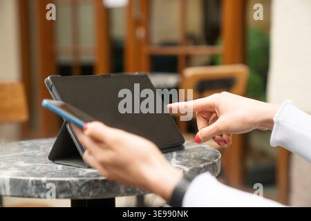 Close-up view of hands interacting with a tablet and smartphone in an outdoor workspace environment. This image is ideal for business, technology, rem Stock Photo