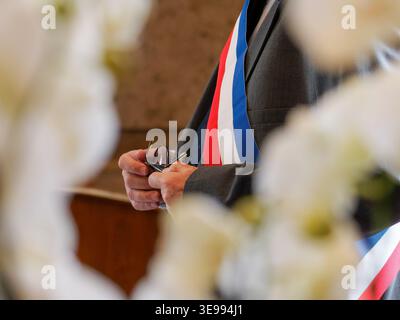 An elected official wearing a French tricolor sash stands with his back ...